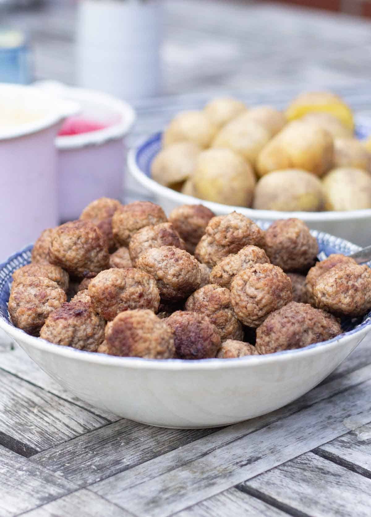 swedish meatballs in a blue and white ceramic bowl beside a ceramic bowl of potatoes