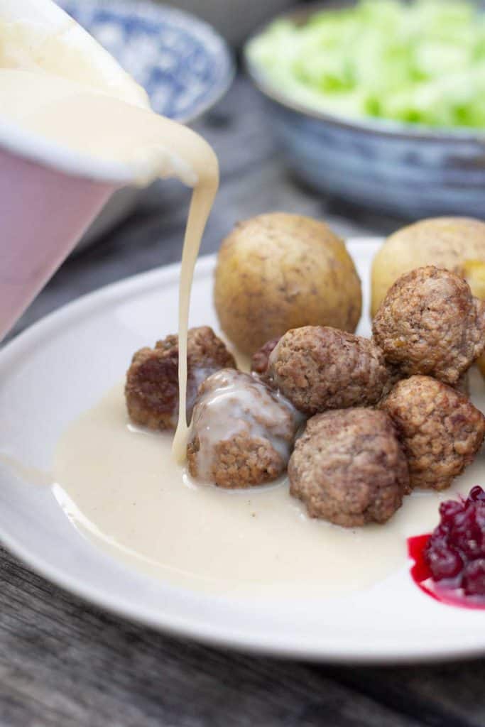 cream sauce being poured over swedish meatballs