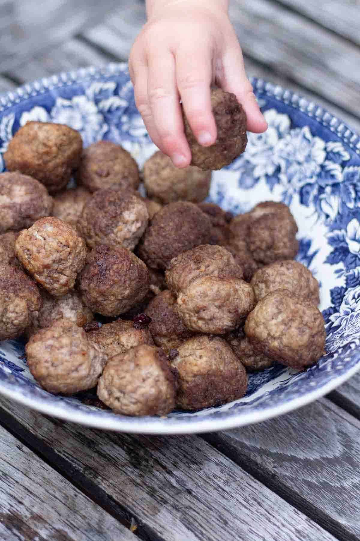 a childs hand taking a swedish meatball rom a bowl