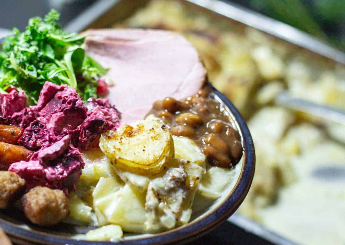 A ceramic plate filled with traditional swddih christmas food, brown beans, beet root salad, meat balls and brown beans