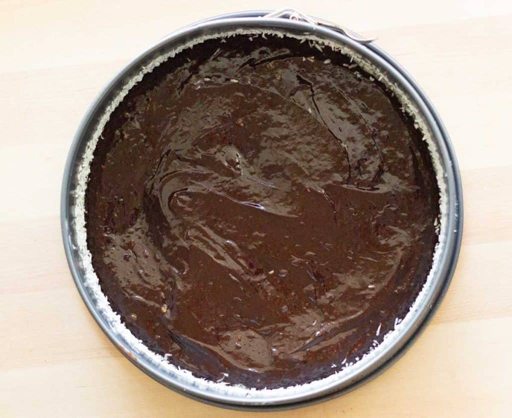 Rich chocolate cake with smooth, shiny frosting in a round baking pan.