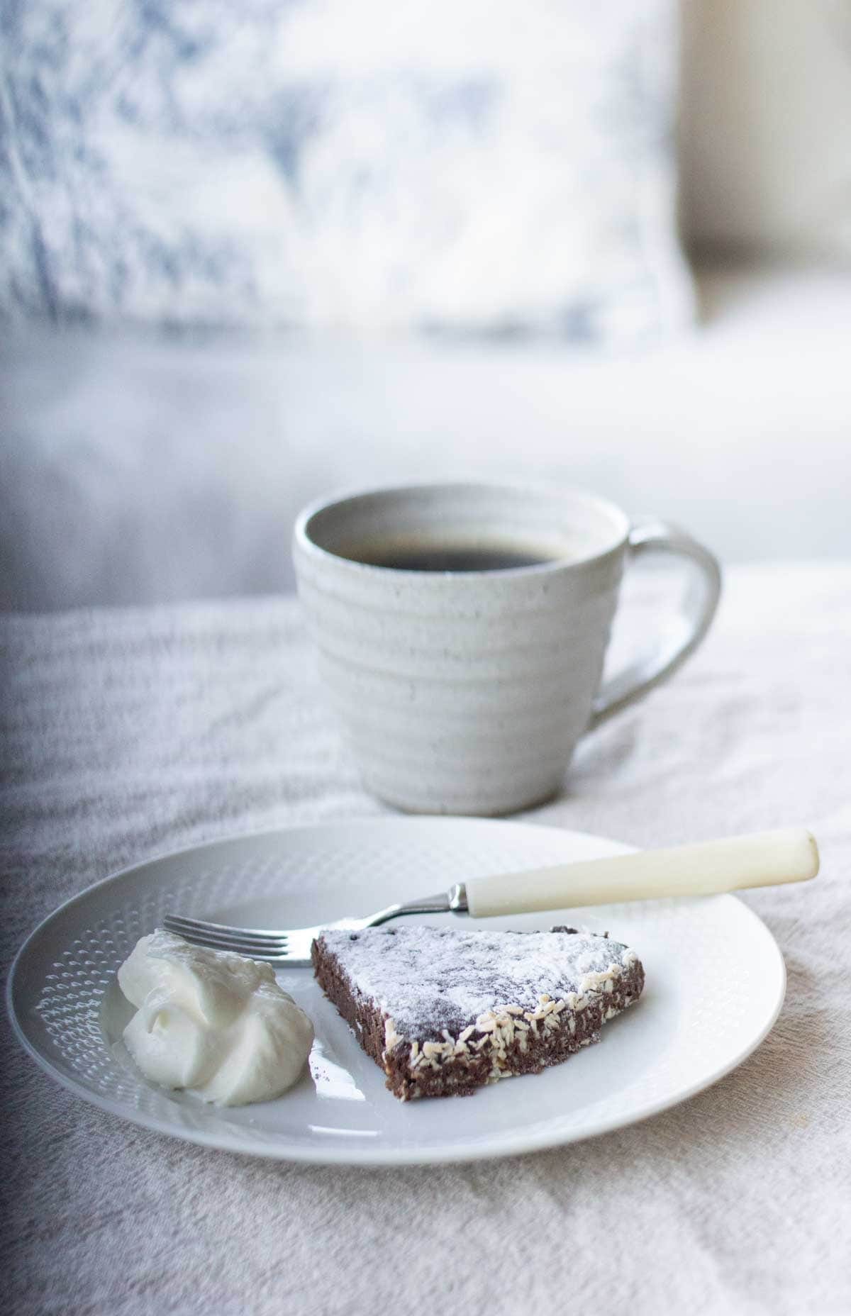 A slice of swedish kladdkaka beside a dollop of whipped cream on a white plate