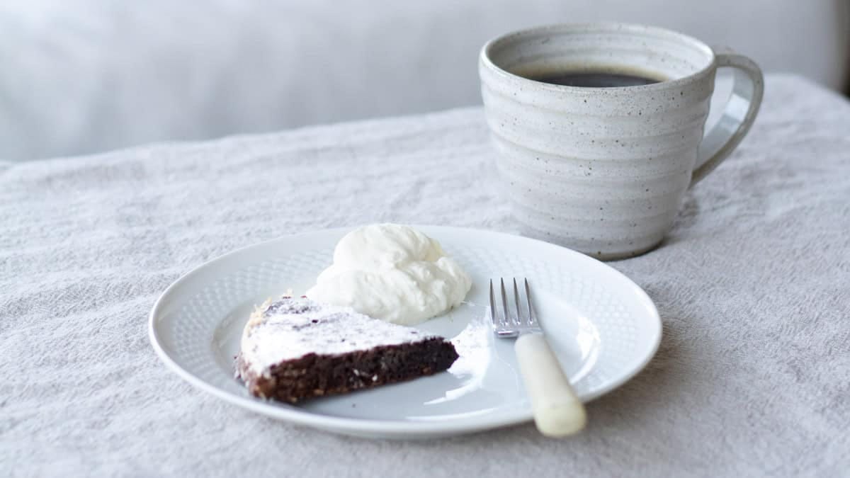 slice of swedish kladdkaka on a white plate beside a dollop of whipped cream.
