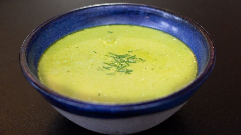 side view of a blue ceramic bowl filled with fresh pea shoot soup and garnished with chopped chive