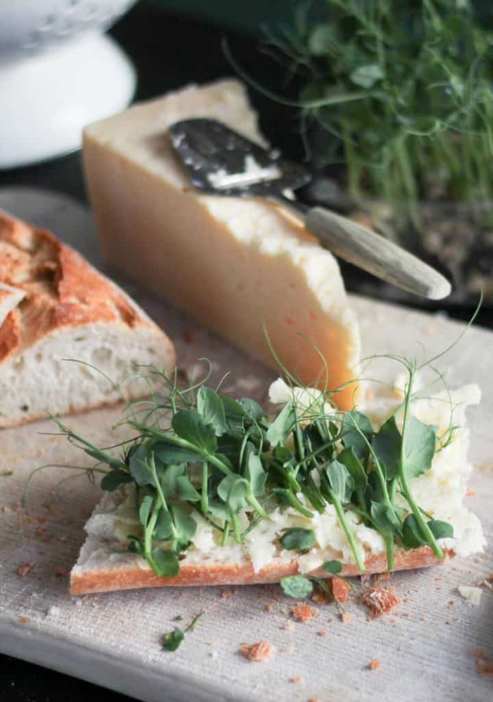 crucnhy baguette, cheee and fresh pea shoots on a wooden chopping board
